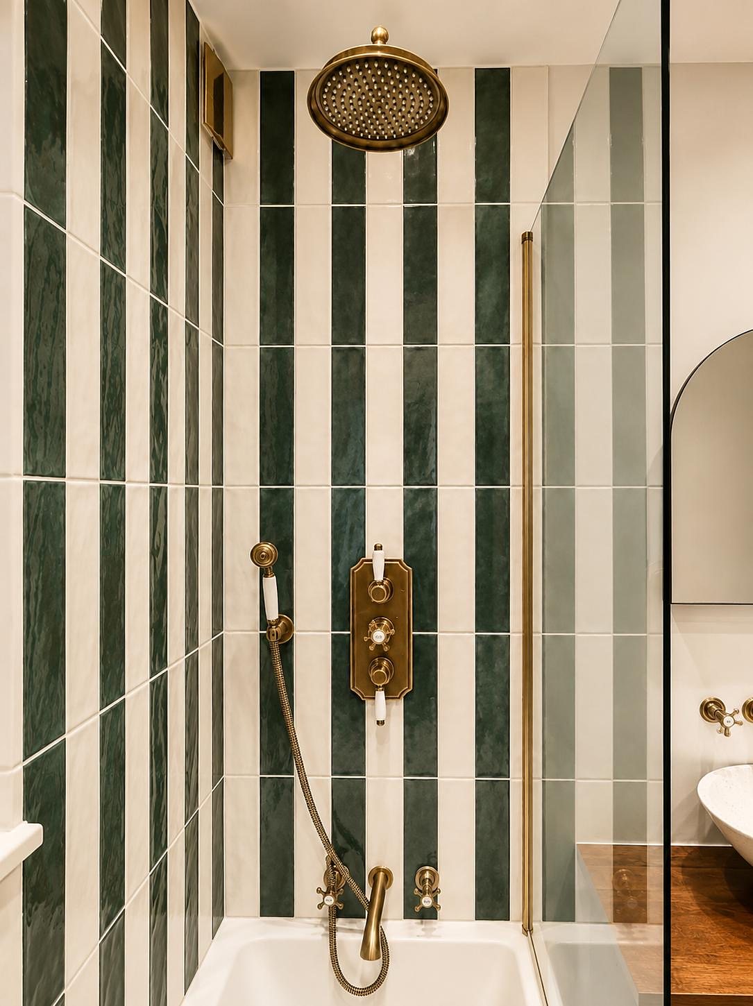 Antique brass shower head and valve against striped tiles