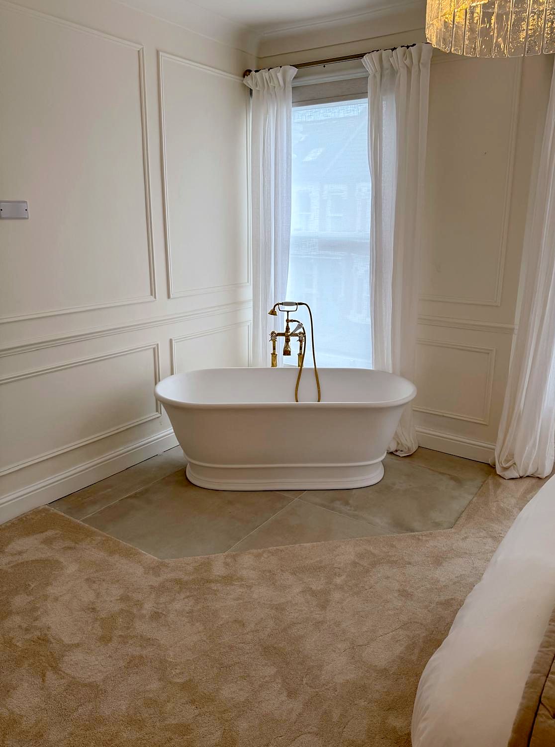 Freestanding bath with brass taps set in a panelled bedroom bay window
