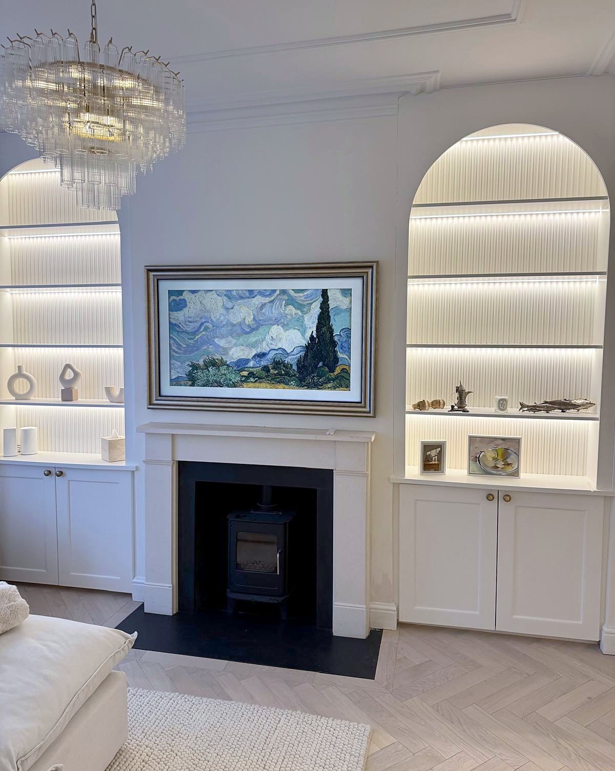 Living room in Brixton with arched alcove shelving lit from behind, a stone fireplace and herringbone oak floor