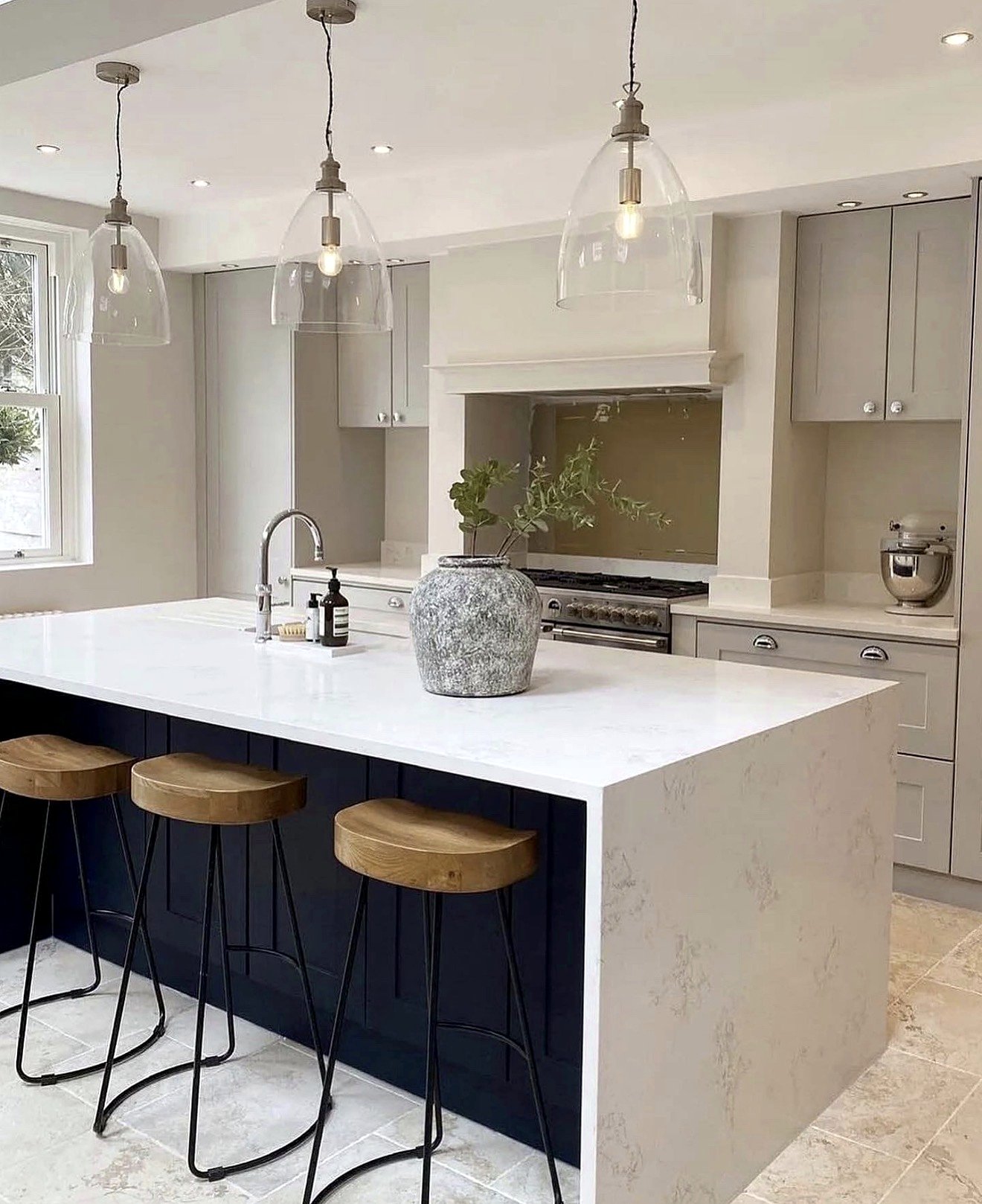 Grey shaker kitchen with a navy island, stone waterfall worktop and glass pendant lights
