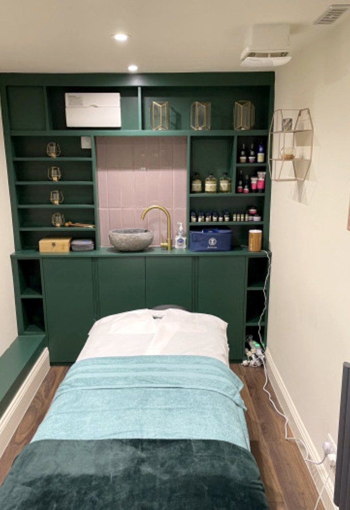 Treatment room with green fitted cabinetry, a stone basin and a treatment bed
